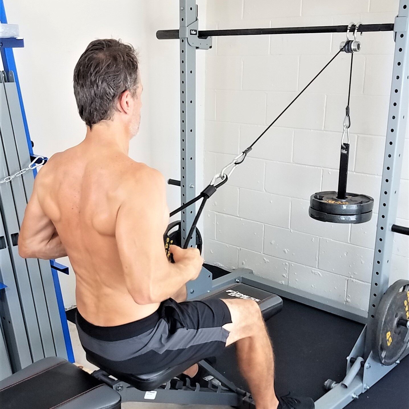 man sitting at weight bench pulling a cable attached to weight