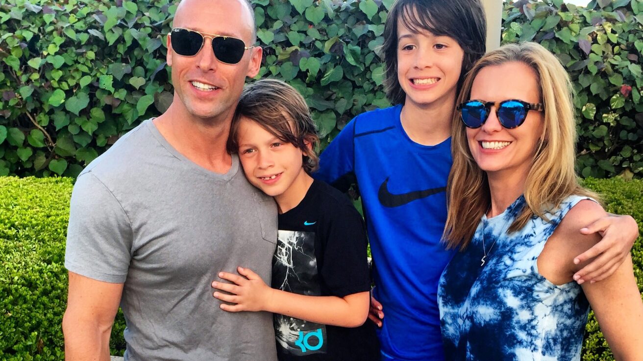 parents and two children standing and smiling in front of a green bush