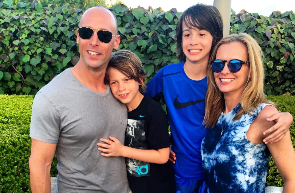 parents and two children standing and smiling in front of a green bush